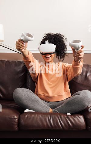 Young happy woman sitting on couch using VR Stock Photo
