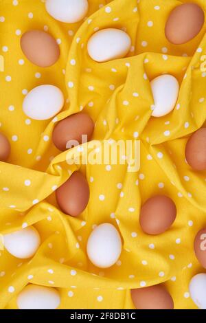 Vertical shot of chicken eggs on yellow textile cloth. Stock Photo