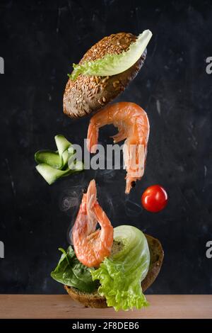 the flying burger with shrimps on black background. Stock Photo