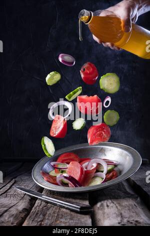 Flying ingredients salad tomatoes cucumbers and onions isolated on a dark background. Rustic style. Stock Photo