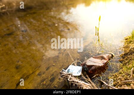 Medical mask and old plastic bottle in a clean water of small river, with sunshine.