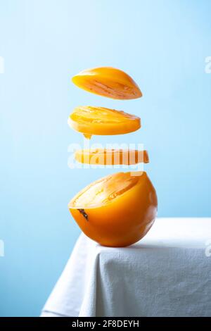 Yellow tomato slices levitating in the air isolated on blue background Stock Photo