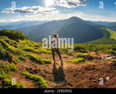 Girl on mountain peak with green grass at sunset in summer Stock Photo