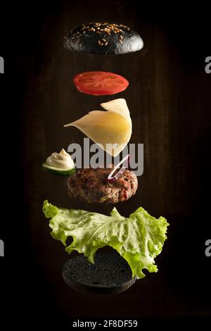 Flying ingredients for homemade burger on dark background. Stock Photo