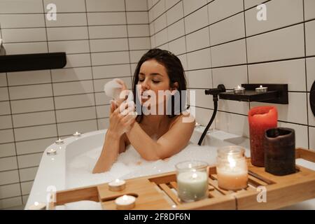 Young woman relaxing in the beautiful bath full of foam decorated with candles. Healthy treatment and enjoyment Stock Photo