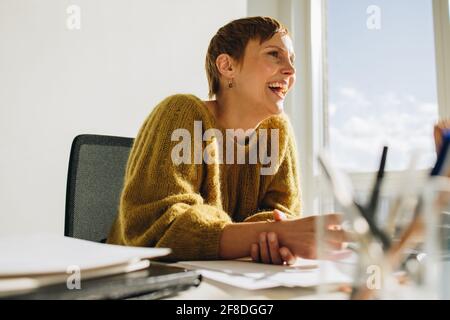 Happy entrepreneur sitting at desk. Cheerful woman looking happy while working in office. Stock Photo