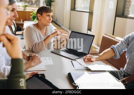Young businesswoman sitting in meeting and sharing project on laptop to colleagues. Woman entrepreneur in business meeting. Stock Photo