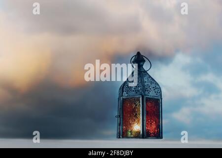 Old burning Morrocan lantern at sunset. Blurred dramatic moody colorful sky and clouds at twilight. Ramadan Kareem greeting card, invitation. Muslim Stock Photo