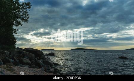 Evening landscape on the White Sea. Shoreline with stone boulders. The sun's rays breaking through the clouds. Cloudy sky over the sea surface. The im Stock Photo