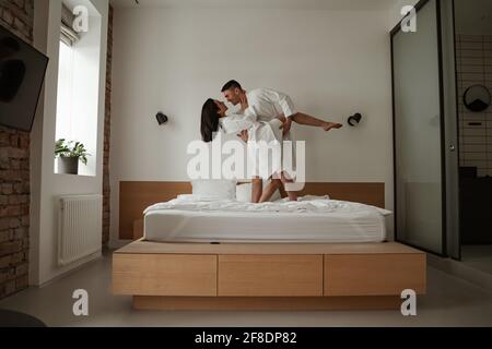 Morning happy young couple in white bathrobes are dancing in bed at home Stock Photo