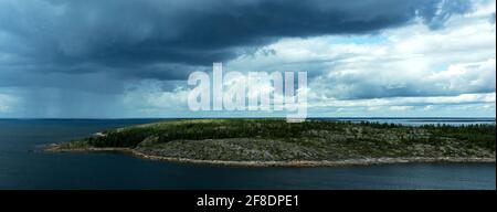 Landscape with an island overgrown with forest and a picturesque cloudy sky in the open sea. Panoramic HDR image. White Sea, Russia. Stock Photo