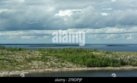 View of the sea and sky from a high point. Harsh northern nature. Rocky island overgrown with forest, dramatic sky with rain clouds. Beautiful view of