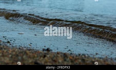 Coastline. Blue sea water, surf. Small waves. Marine wet pebbles in close-up. Taken in a low key. Background image. low depth of field Stock Photo