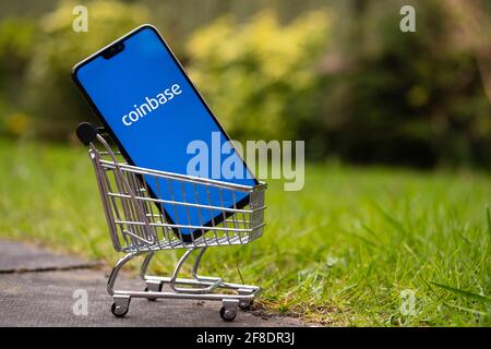 Coinbase IPO concept. Coinbase app logo seen on the screen on smartphone which is placed into miniature shopping trolley. Stafford, United Kingdom, Ap Stock Photo