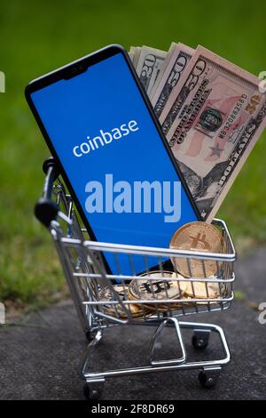 Coinbase IPO concept. Coinbase app logo seen on the screen on smartphone which is placed into miniature shopping trolley with dollars and bitcoins. St Stock Photo