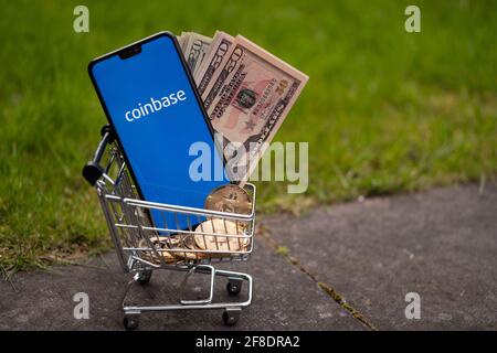 Coinbase IPO concept. Coinbase app logo seen on the screen on smartphone which is placed into miniature shopping trolley with dollars and bitcoins. St Stock Photo