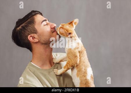 Man holding and kissing muzzle cute Devon rex cat Stock Photo