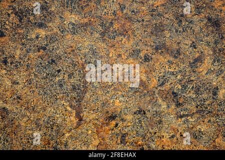 Golden-black granite, polished surface of natural stone with dark small inclusions close-up. Background, pattern, texture. Stock Photo