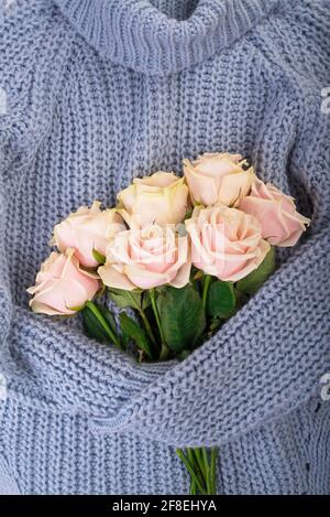 White winter sweater with a bouquet delicate roses. Spring and winter mood composition. Flat lay, top, top view. Stock Photo