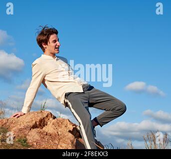 Side view of a young Spanish handsome male leaning on the rock against the cloudy blue sky Stock Photo