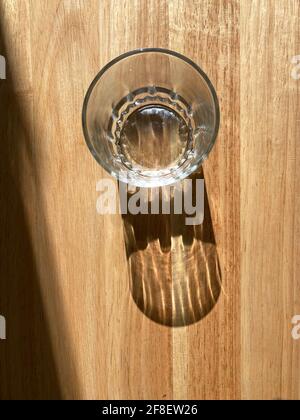 Empty glass cup on a wooden table with its shadow showing. Stock Photo