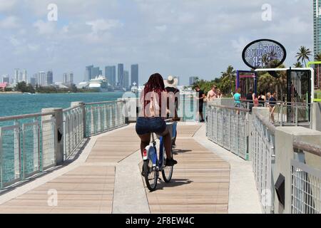 Woman and man riding bike on the South Pointe Pier in Miami Beach, South Beach in Florida during spring break. Stock Photo