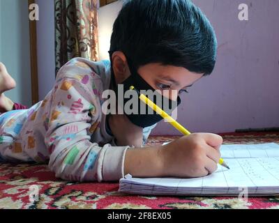 Masked students  reading and writing their school work at home during the pandemic coronavirus. Online classes are common due to covid 19.