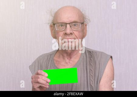 Old retired bald man with eyeglasses in gray shirt is blank in his hand.