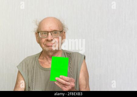 Old retired bald man with eyeglasses in gray shirt is blank in his hand.