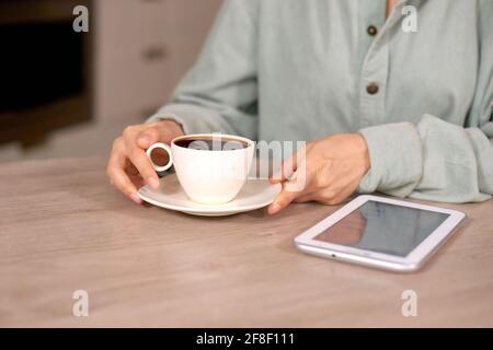 closeup woman holding coffee cup and white tablet on table Stock Photo