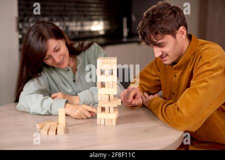Happy couple playing Jenga while sitting in kitchen at home, having fun together Stock Photo