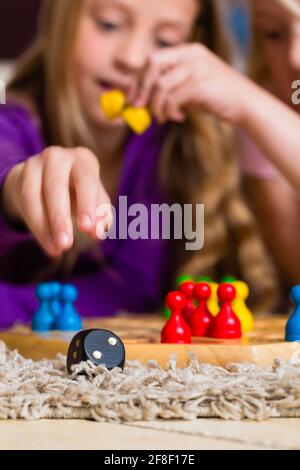 Family - two sisters - playing board game ludo at home on the floor, focus on dice in the front Stock Photo
