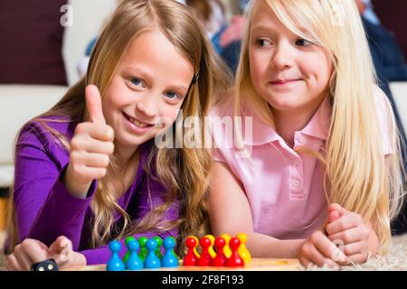 Family - two sisters - playing board game ludo at home on the floor, focus on dice in the front Stock Photo