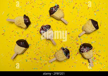 some marzipan sweets with wooden stick on a yellow surface Stock Photo