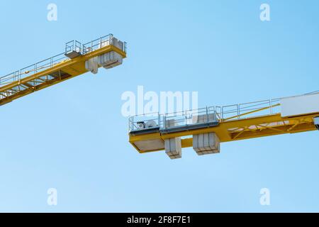 Two arms of yellow construction cranes with concrete weights face each other. Stock Photo