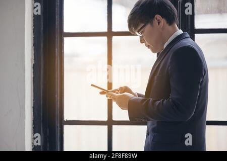 Handsome businessman checking emails on the phone near the window in the loft interior studio Stock Photo
