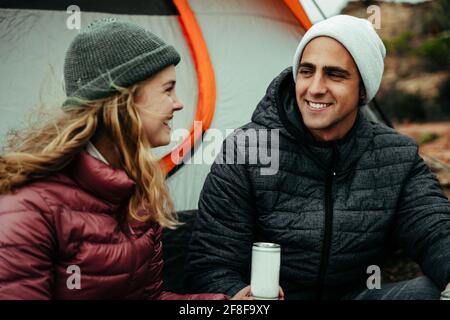 Caucasian couple smiling at each other chatting while camping in mountain Stock Photo