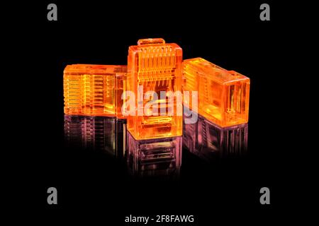 Connector rj-45. Three orange transparent connectors rj45 for network and internet. Close up macro isolated on black background with reflection. Stock Photo