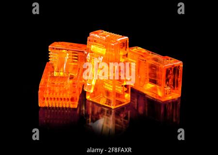Connector rj-45. Four orange transparent connectors rj45 for network and internet. Close up macro isolated on black background with reflection. Stock Photo