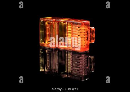 Connector rj-45. Orange transparent connector rj45 for network and internet. Close up macro isolated on black background with reflection. Stock Photo
