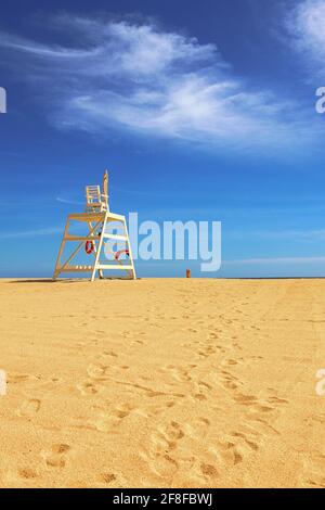 Lifeguard chair on the sandy beach overlooking the ocean, with blue sky background Stock Photo