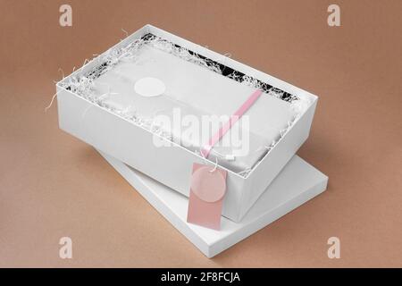 mock-up pink blank tag for brand or logo on white tissue paper, unpacking white box with clothes on beige paper texture background Stock Photo