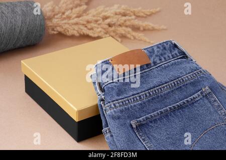 close-up leather empty tag or label on the back pocket of blue jeans on a vase of spool yarn with dry pampas grass and black golden box