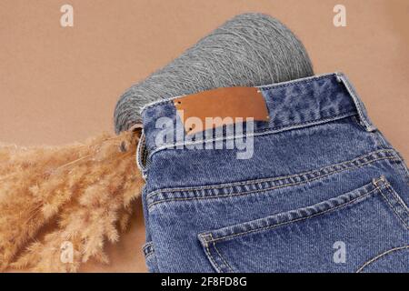 close-up leather empty tag or label on the back pocket of blue jeans on a vase of spool yarn with dry pampas grass