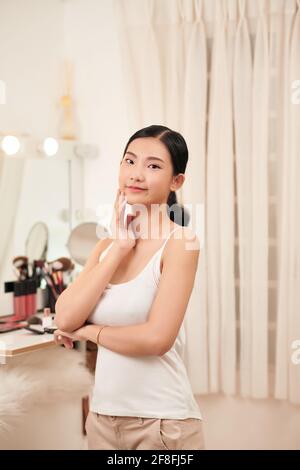 Beautiful young woman is touching her face and smiling while looking at the mirror Stock Photo