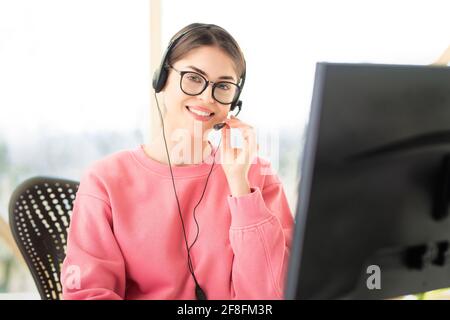 Young businesswoman in headset speaking by conference call while looking at camera. Home office. Stock Photo