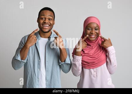 Smiling black man and woman pointing at their white teeth Stock Photo