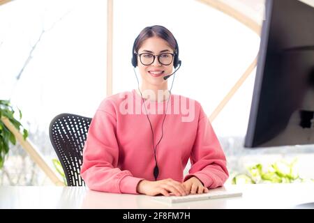 Young businesswoman in headset speaking by conference call while sitting at desk. Home office. Stock Photo