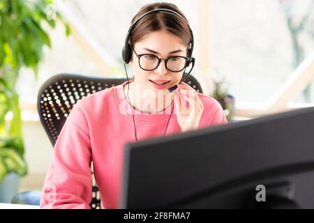 Young businesswoman in headset speaking by conference call while looking at computer. Home office. Stock Photo