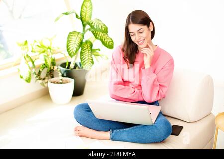 Smiling young woman sitting on the sofa at home and having video call. Stock Photo